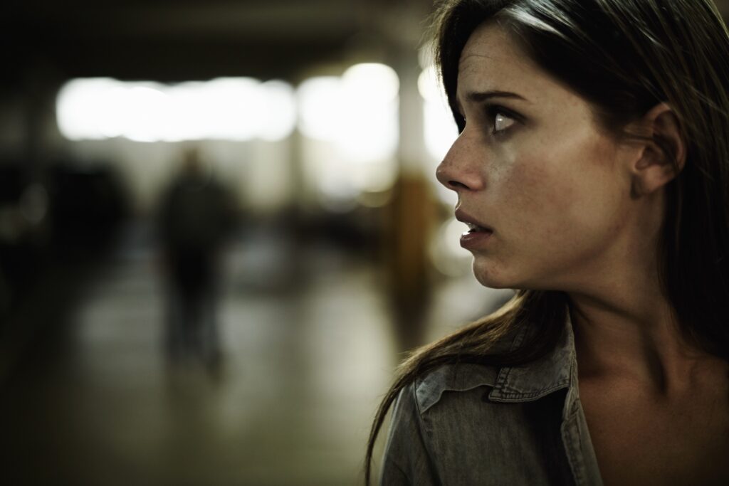 A young woman in a parking lot looking concerned as someone follows her